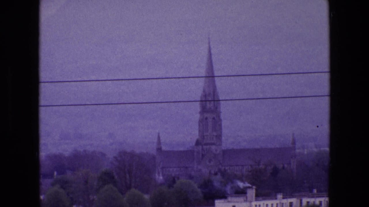 Tall church spire above rooftops with overhead wires and trees in the foreground.