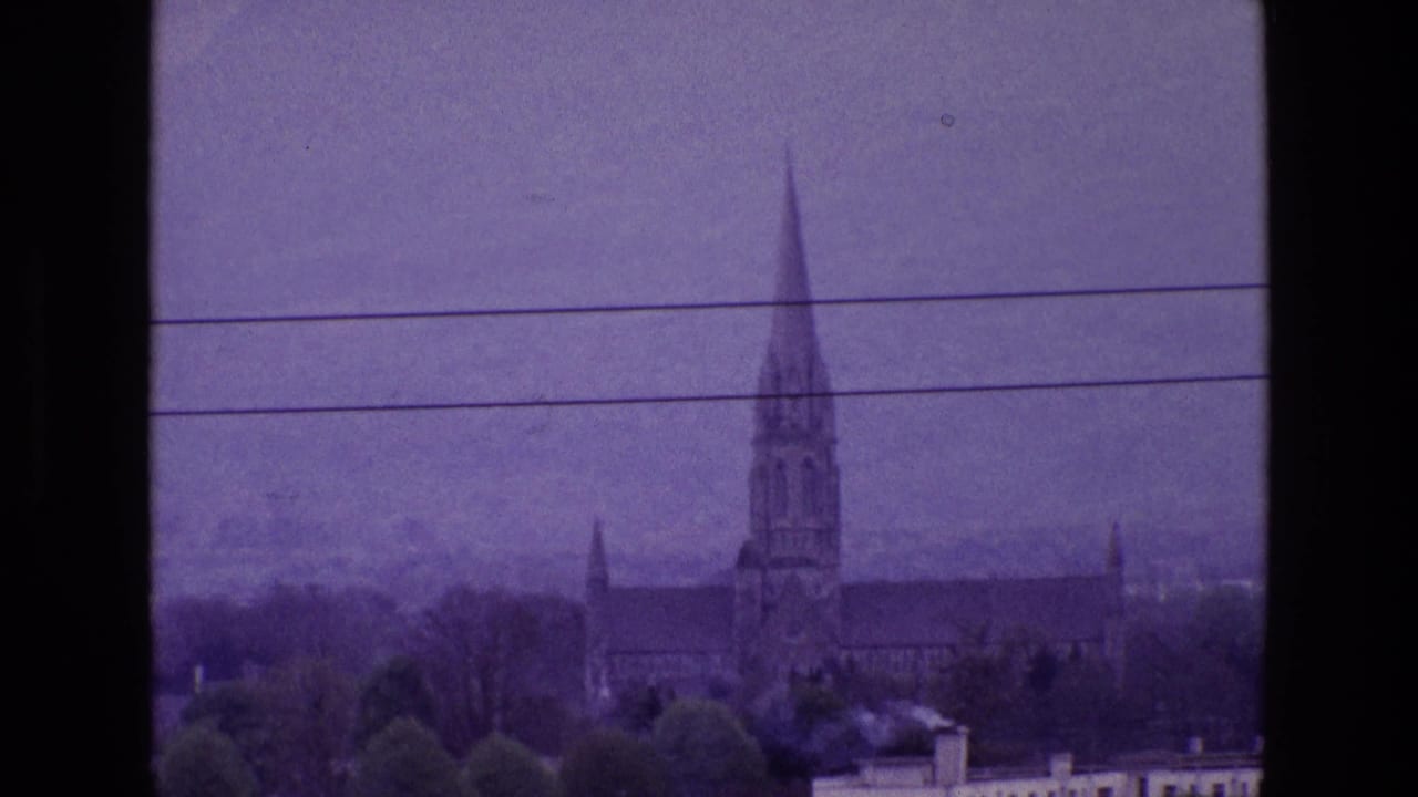 Distant Irish town view from 1969 with a church spire, rooftops, trees, and utility wires across a purple-tinted sky.