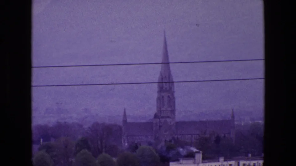 Distant Irish town view from 1969 with a church spire, rooftops, trees, and utility wires across a purple-tinted sky.