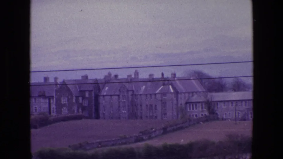Elevated 1969 Ireland town view with stone buildings, chimneys, open ground, trees, and utility wires in the foreground.