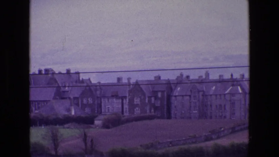 A distant 1969 Ireland countryside view with stone or brick houses above open pasture and overhead utility lines.
