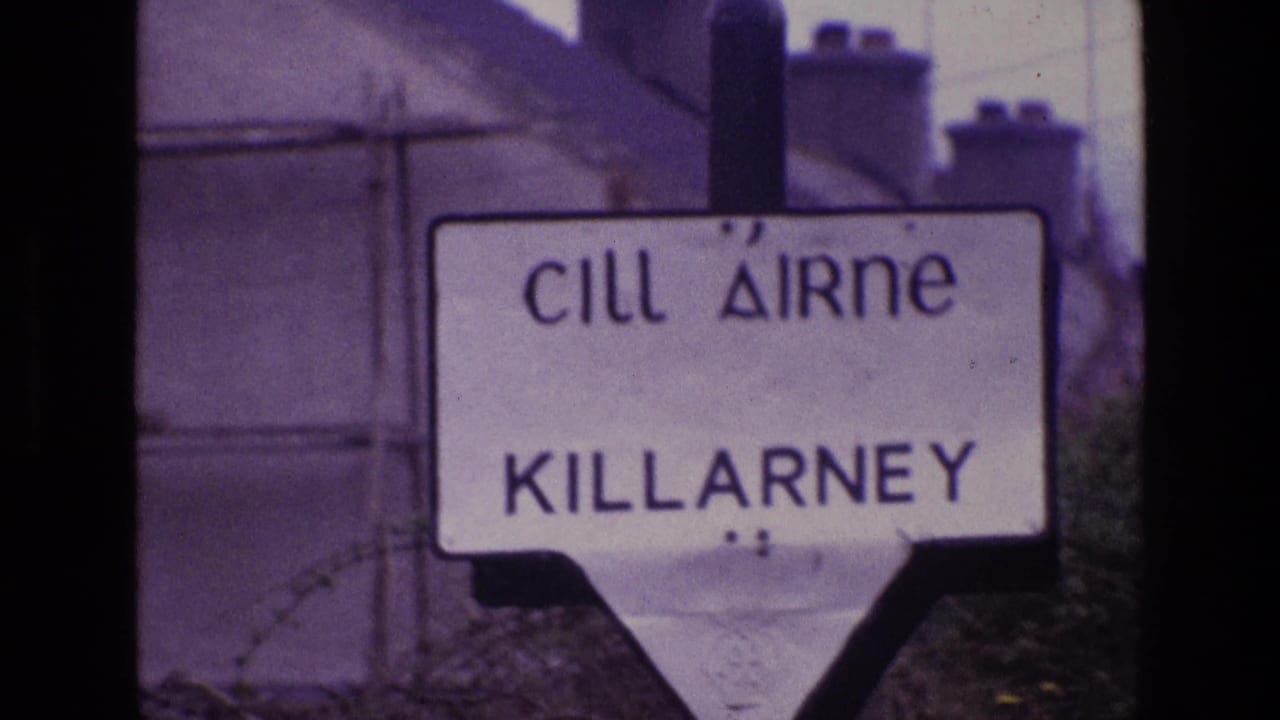 1969 Ireland home-movie frame showing a bilingual Cill Airne Killarney road sign behind foreground barbed wire.