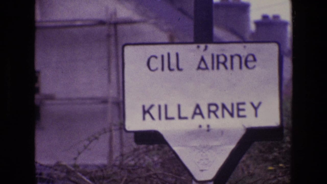 1969 Ireland frame of a white Cill Airne Killarney sign, softly focused with barbed wire crossing the foreground.