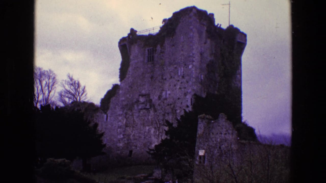 1969 Ireland 8mm frame of a crumbling stone tower ruin, ivy-covered sections, leafless trees, and overcast sky.