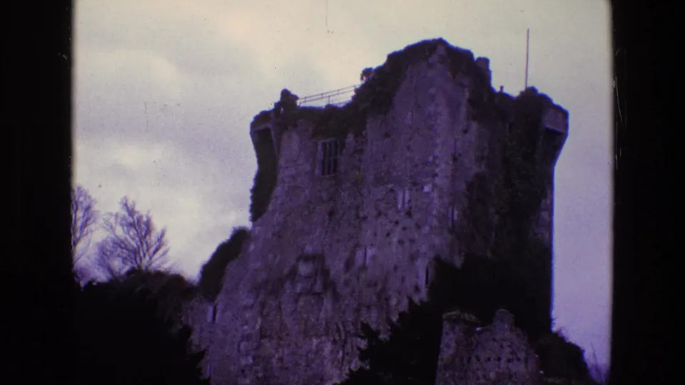 1969 Ireland 8mm frame showing a closer handheld view of the castle ruin, rough masonry, ivy, bare trees, and gray sky.