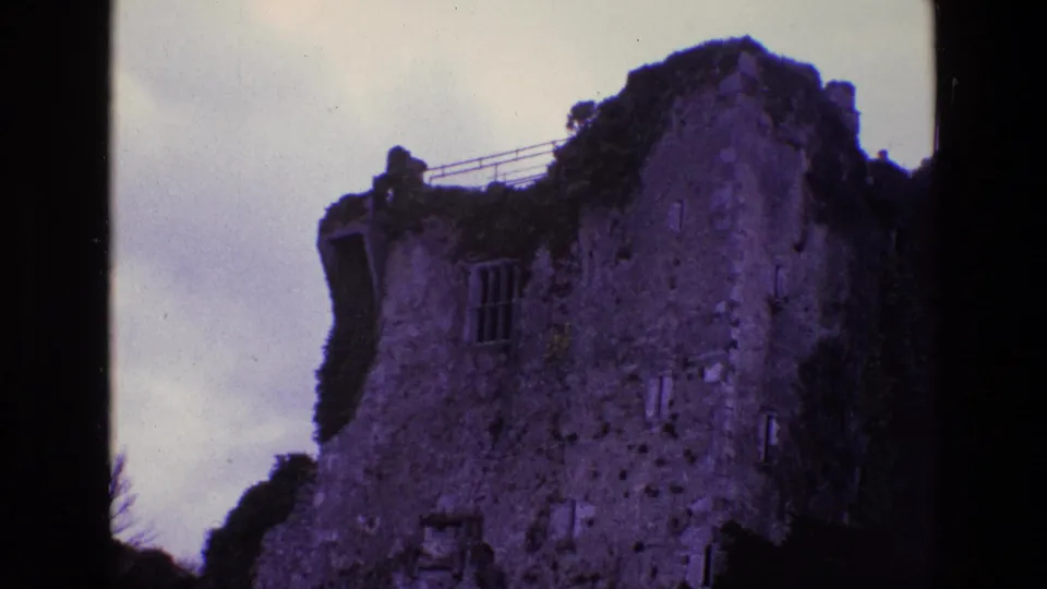 1969 Ireland 8mm frame of a tall weathered castle ruin with a visible window opening, ivy growth, and overcast sky.