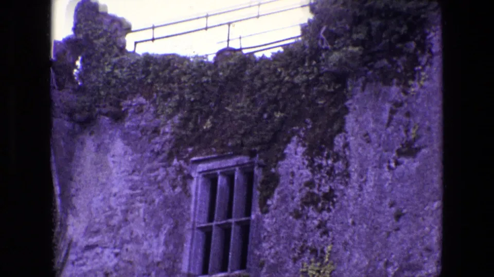 1969 Ireland 8mm frame with a closer view of an ivy-covered stone ruin, barred window, roof railing, and purple color cast.