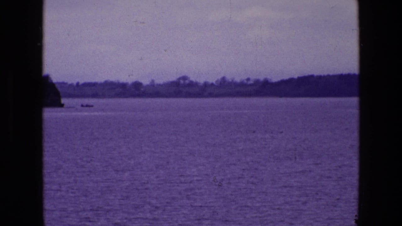 Ireland lake landscape on 8mm film, with open water, distant trees, a small boat near the horizon, and dark window framing in the foreground.