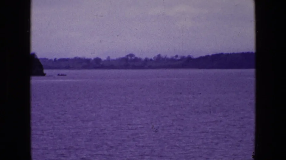 Ireland lake landscape on 8mm film, with open water, distant trees, a small boat near the horizon, and dark window framing in the foreground.