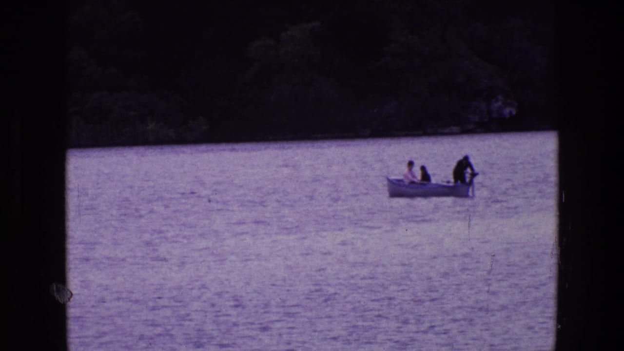 1969 Ireland 8mm frame showing three people in a small motorboat on calm lake water, with one person near the stern motor.