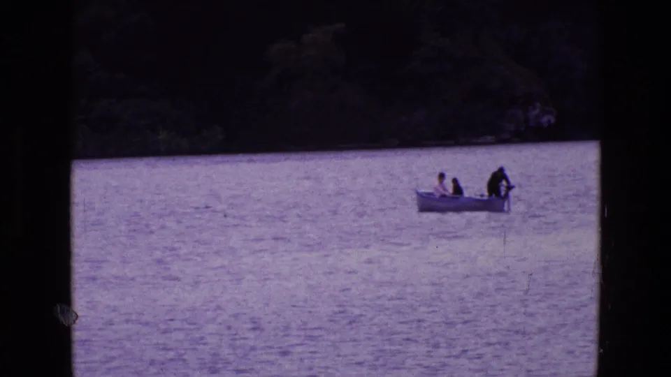 1969 Ireland 8mm frame showing three people in a small motorboat on calm lake water, with one person near the stern motor.
