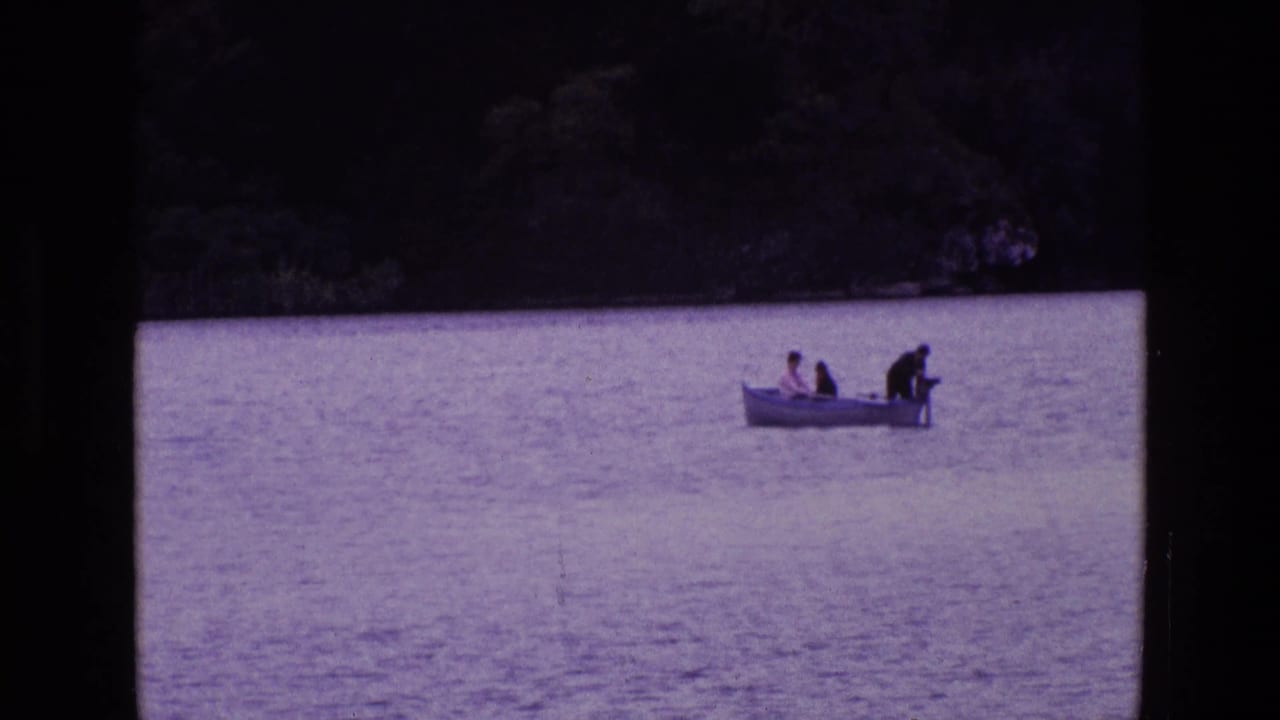 Small boat farther across the lake with three people aboard and trees in the background.