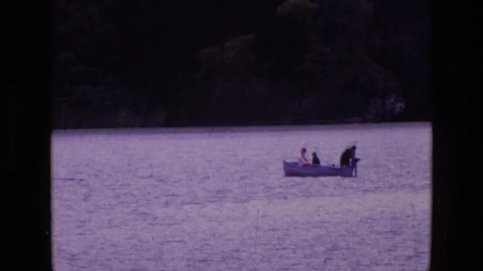 1969 Ireland 8mm still showing a small motorboat with three people on a lake, framed by dark shore and visible film grain.