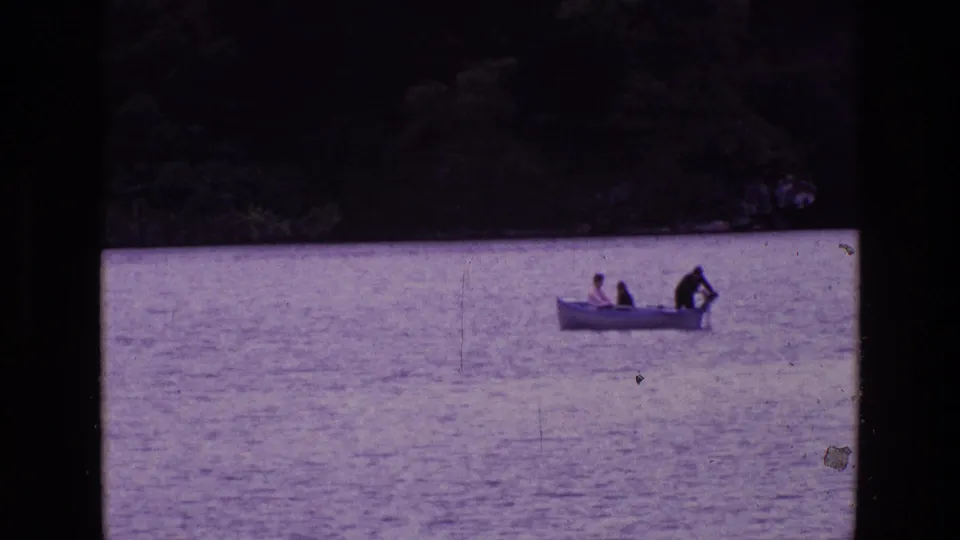 1969 Ireland frame of three people in a small motorboat, with one person appearing to work near the stern motor on calm water.