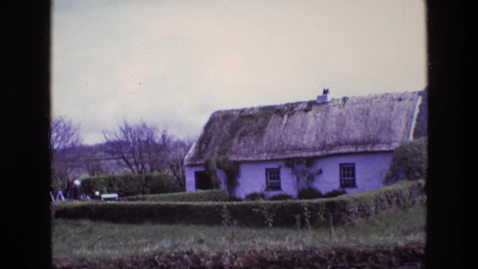 White thatched-roof cottage behind hedges in rural Ireland, captured on 8mm film in 1969.