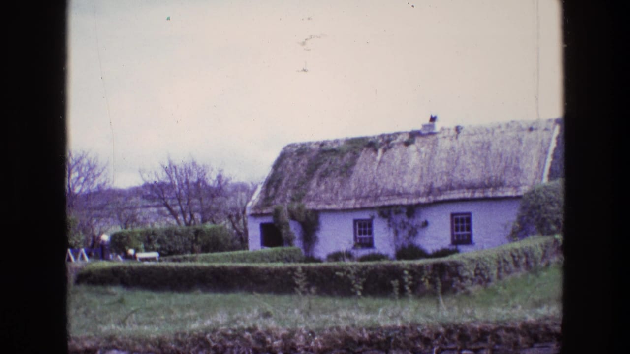 1969 Ireland 8mm frame showing a white thatched cottage behind trimmed hedges, with bare trees and low hills in the background.
