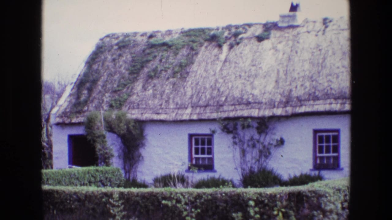 1969 Ireland view of a traditional thatched cottage with white walls, dark window frames, clipped hedge, and weathered mossy roof areas.