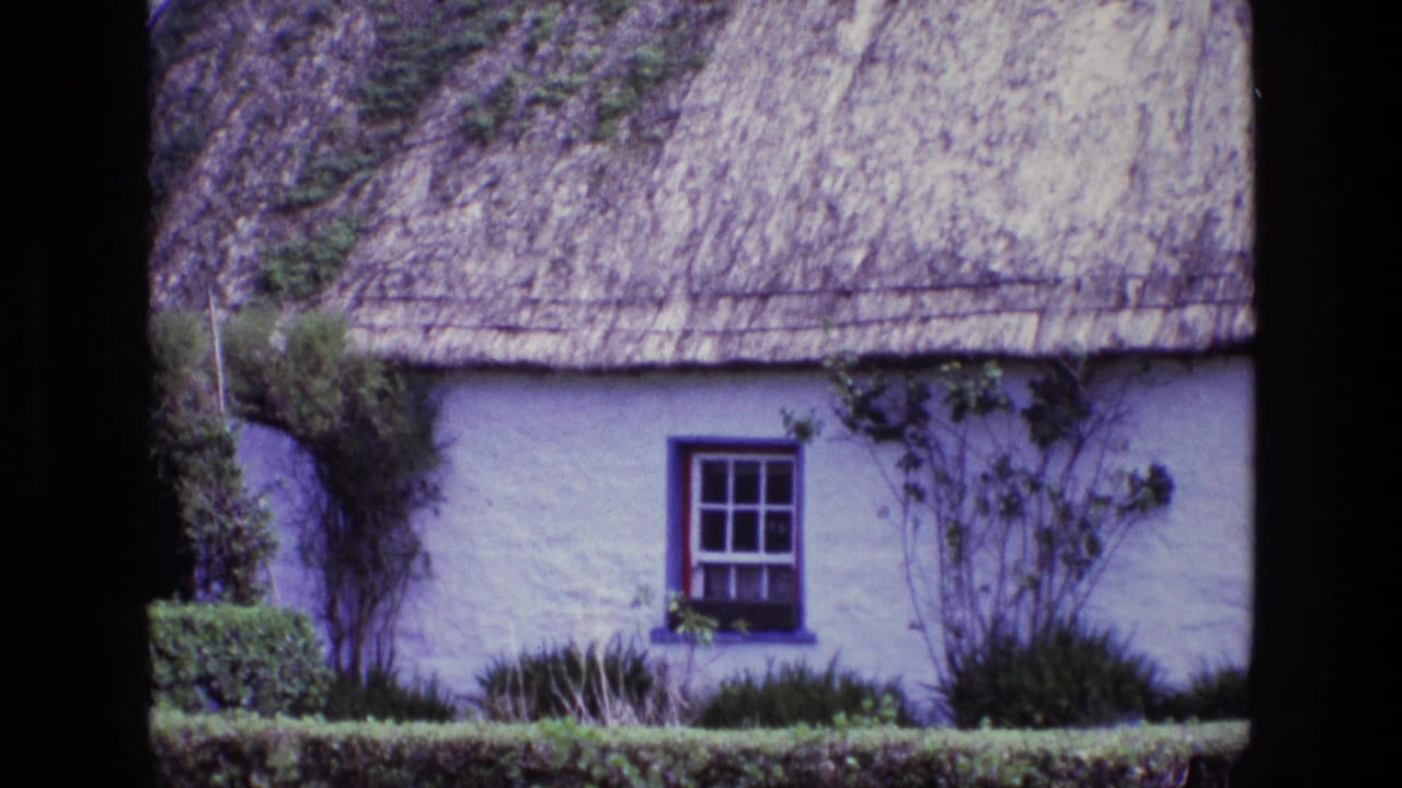 1969 Ireland frame with the thatched roof and blue-framed cottage window centered among hedges and climbing plants.