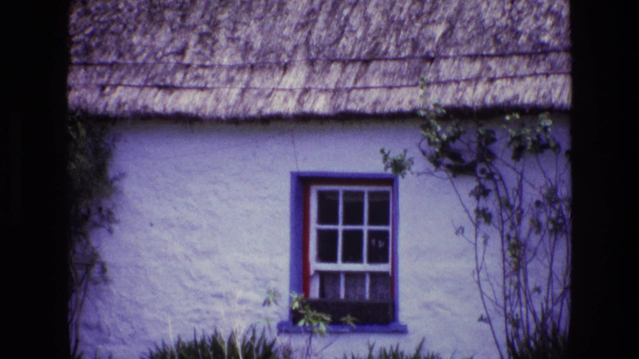 1969 Ireland 8mm frame showing a whitewashed cottage exterior with a red-trimmed window, blue surround, ivy, and thatched roof edge.