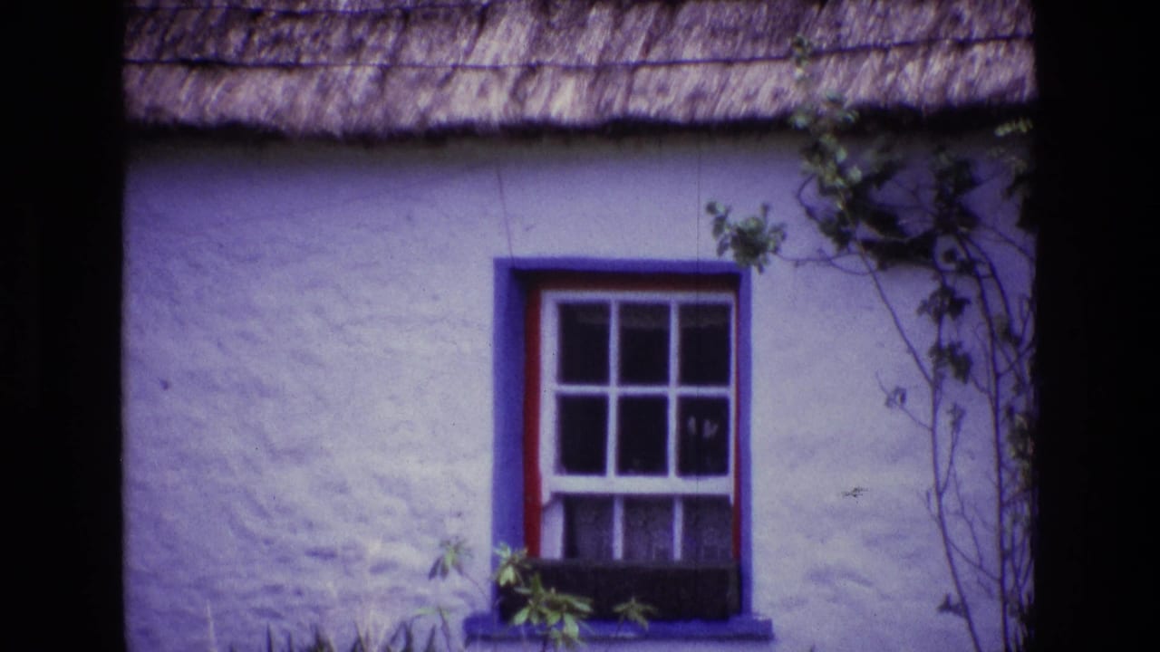 1969 Ireland frame with the camera closer to a red-trimmed cottage window set in a white wall under a thatched roof.