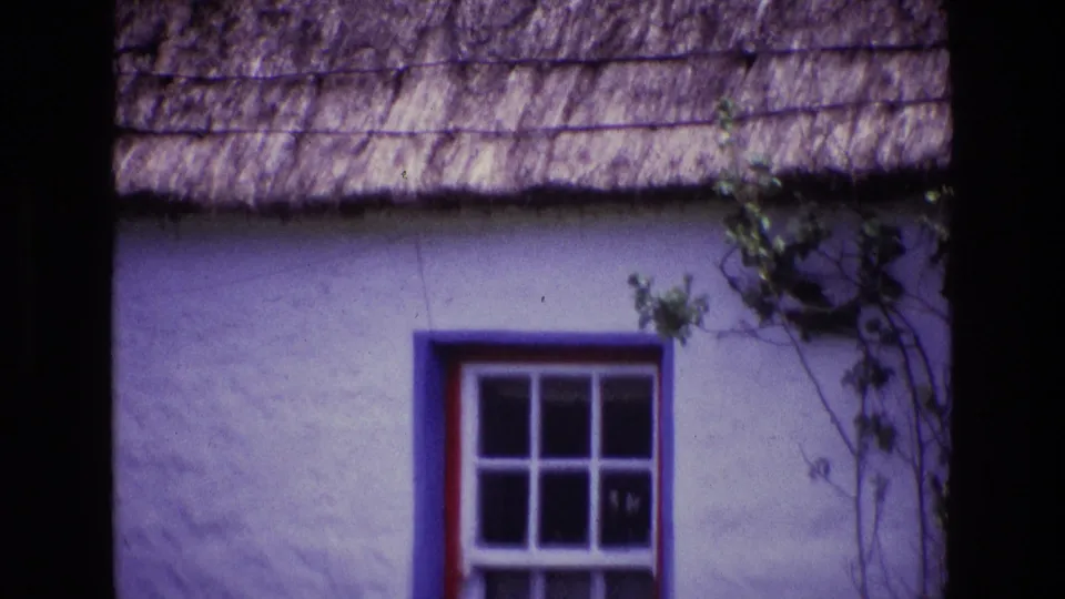 1969 Ireland 8mm frame showing a thatched cottage facade as the zoom holds near the red-trimmed window and white wall.