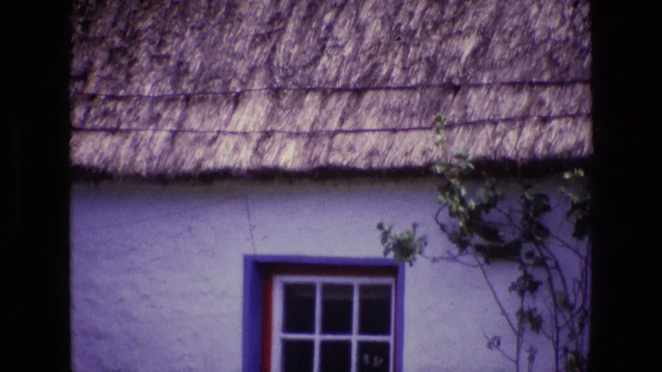 Final 1969 Ireland frame with the zoom closest to the red-trimmed window, blue surround, whitewashed wall, ivy, and thatched roof.