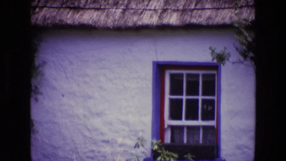 1969 Ireland 8mm view of a traditional cottage window, whitewashed wall, roof thatch, painted trim, and planter box.
