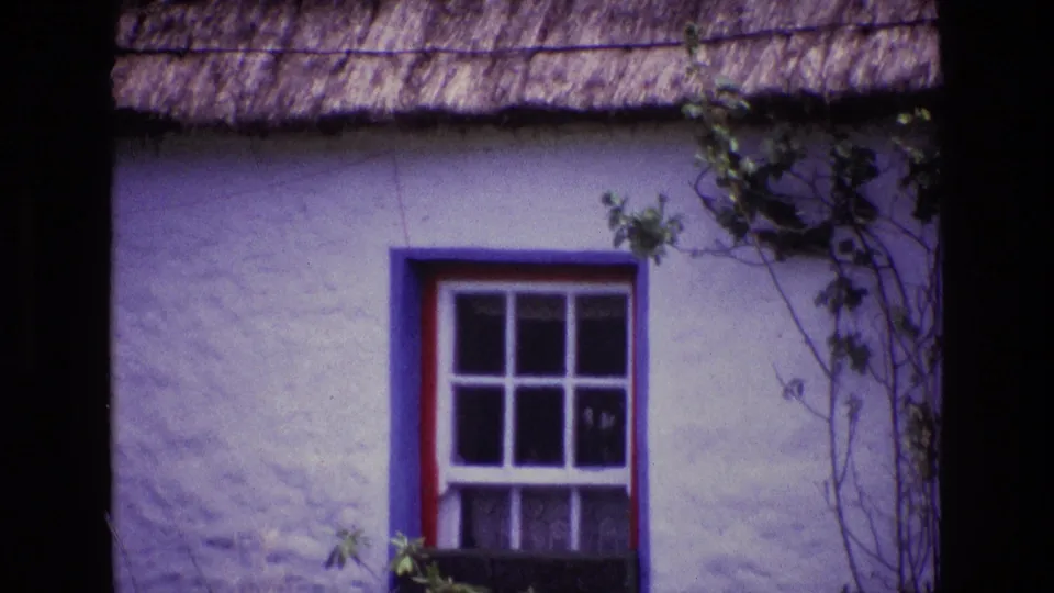 1969 Ireland 8mm frame showing a whitewashed thatched cottage exterior with a blue window frame, red trim, and climbing vines.