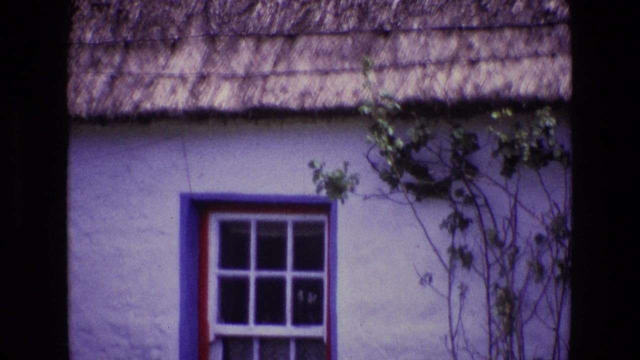 1969 Ireland home-movie still of a thatched cottage facade with blue window trim, red edging, white wall, and vines near the eaves.
