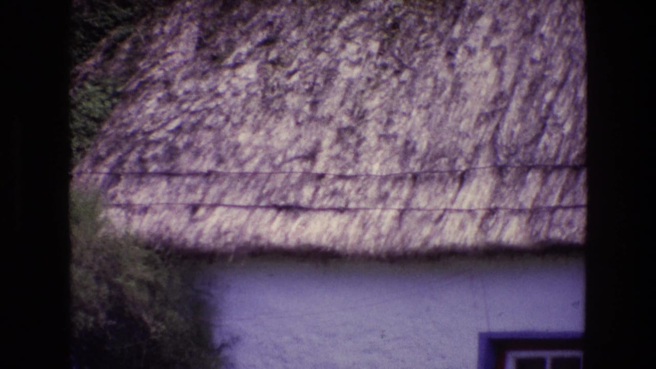 1969 Ireland 8mm frame showing a whitewashed wall, small window edge, and heavy sod or thatch roof with vegetation above.