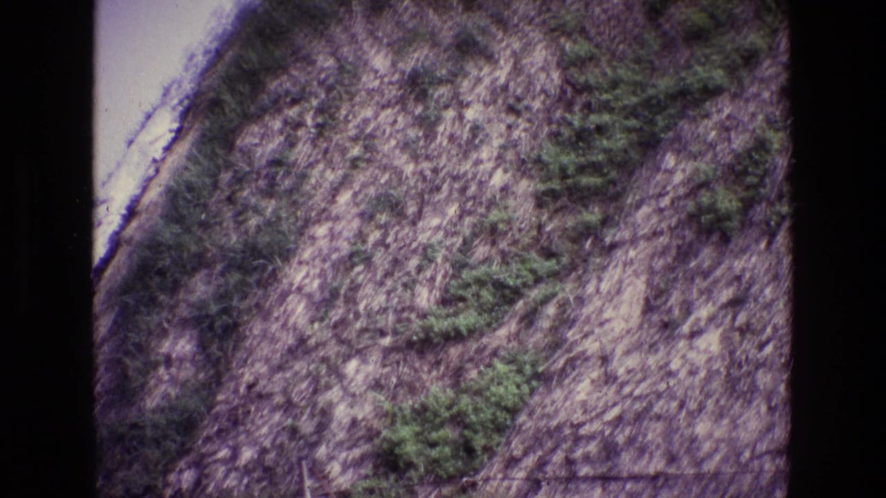 1969 Ireland home-movie frame showing a steep rocky hillside with patches of green shrubs and soft, faded 8mm color.