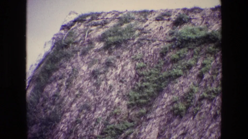 Faded 8mm home-movie view from 1969 Ireland showing rocky hillside terrain with scrubby green vegetation.