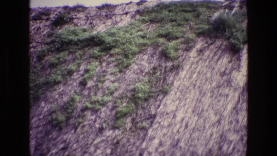 1969 Ireland 8mm frame showing an eroded hillside with green growth and what appears to be wire or fencing along the upper edge.