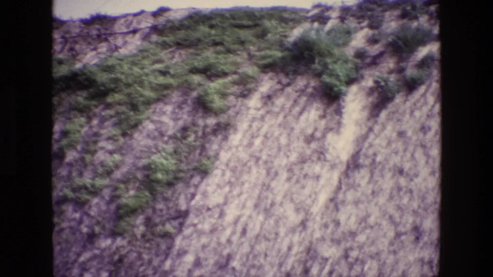 1969 Ireland 8mm frame of a steep pale cliff face with scattered vegetation and visible dark borders from the film scan.