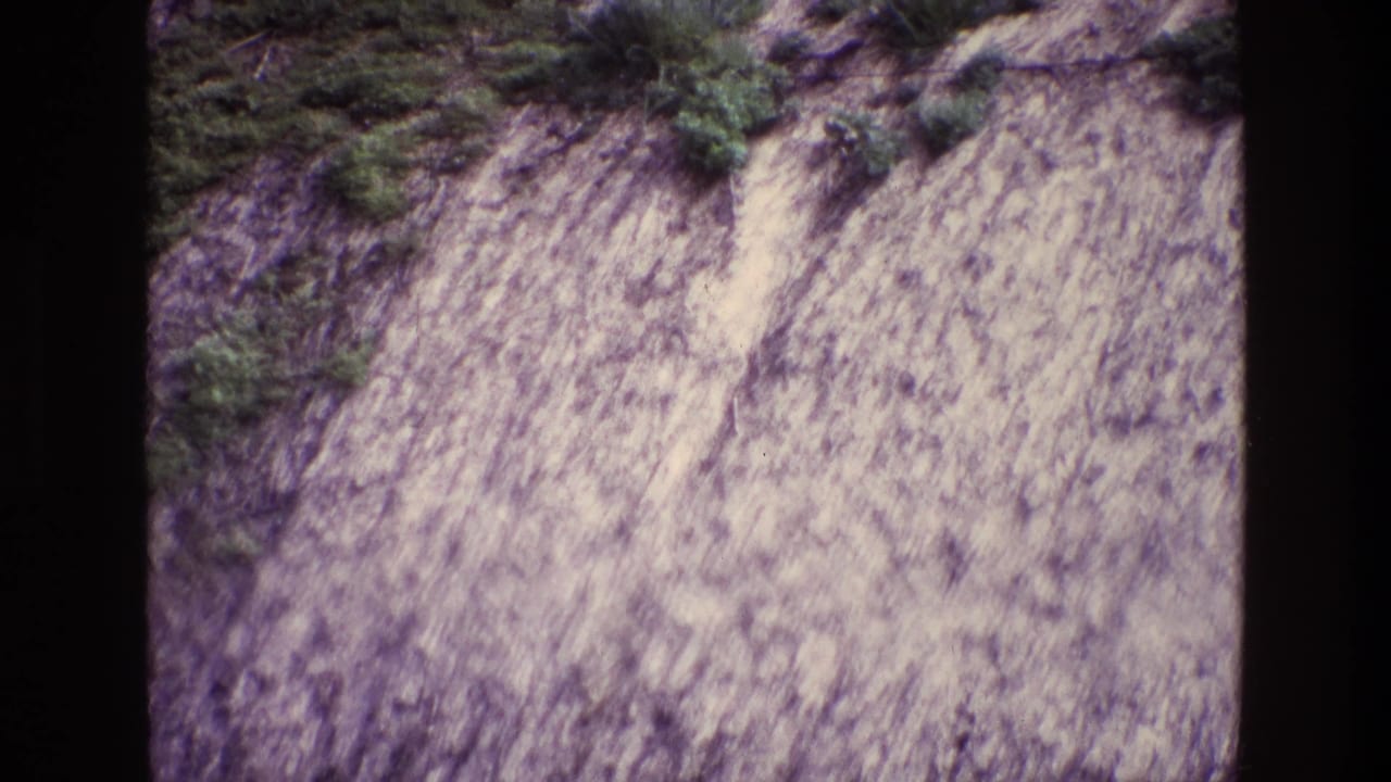 Steep pale rock face with scattered shrubs and grass along the top.