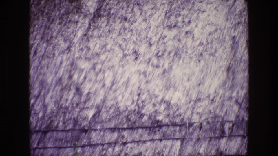1969 Ireland home-movie frame of a pale rocky hillside, sparse upper greenery, and dark linear marks near the bottom.