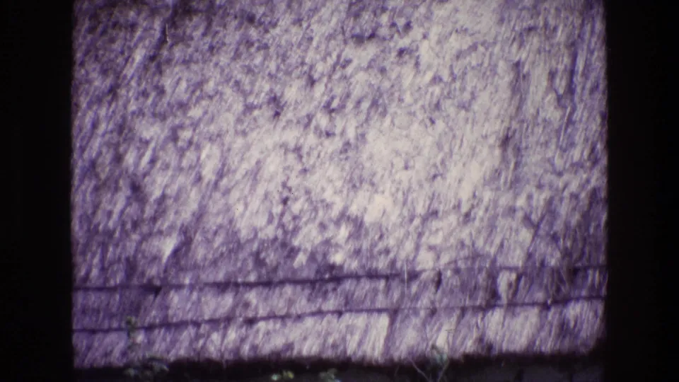 1969 Ireland 8mm frame showing a textured thatched roof above a pale cottage wall, with a strong purple film cast.