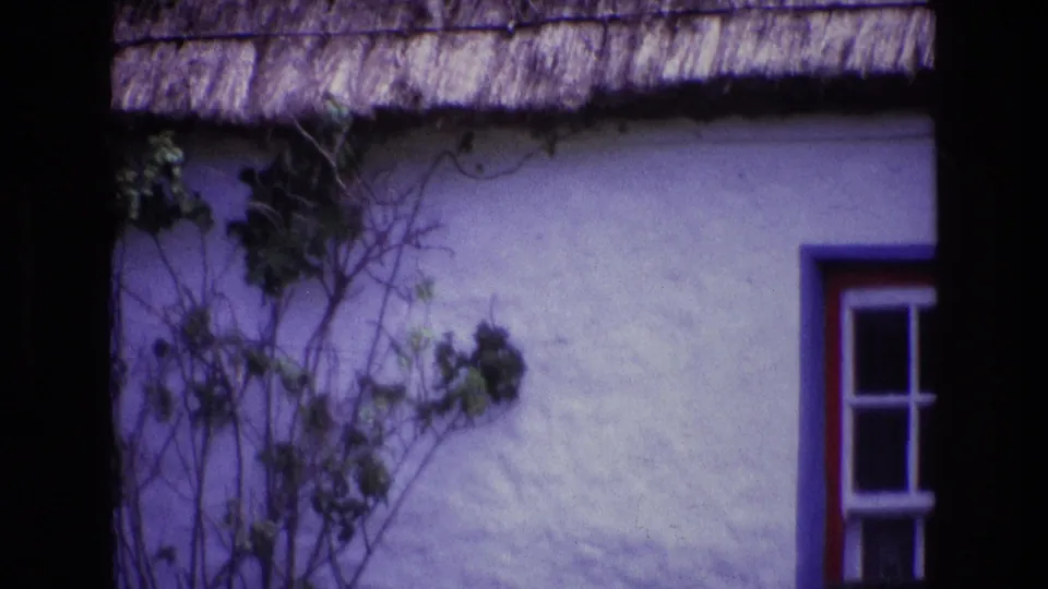 1969 Ireland 8mm frame showing a whitewashed cottage exterior with thatched roof edge, climbing vines, and a red and blue trimmed window partly visible.