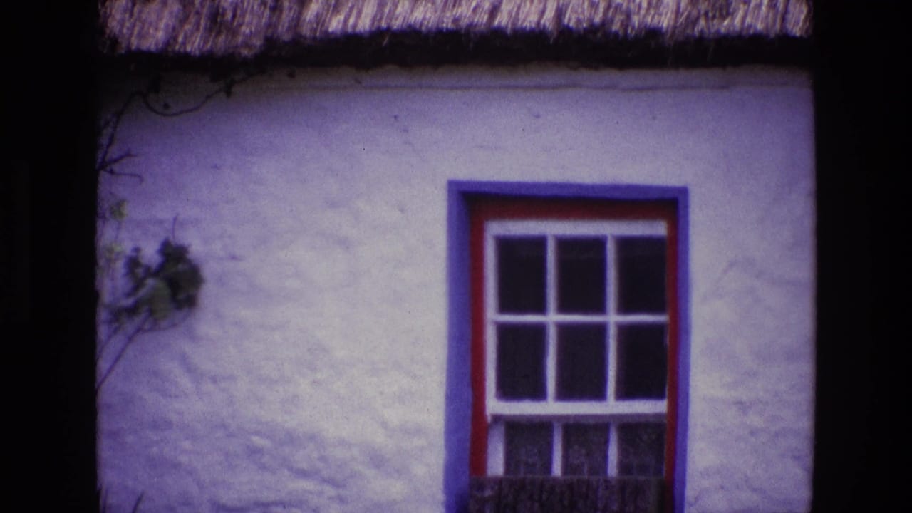 1969 Ireland home-movie frame showing a painted cottage window set in a white textured wall below thatch.