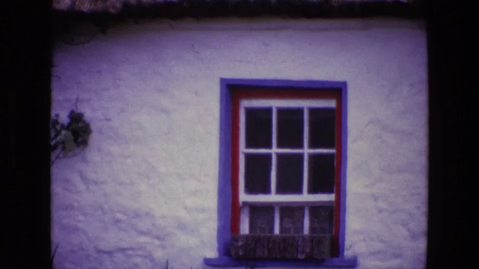 Close 8mm view of a traditional Irish cottage window with colored trim and textured white wall.