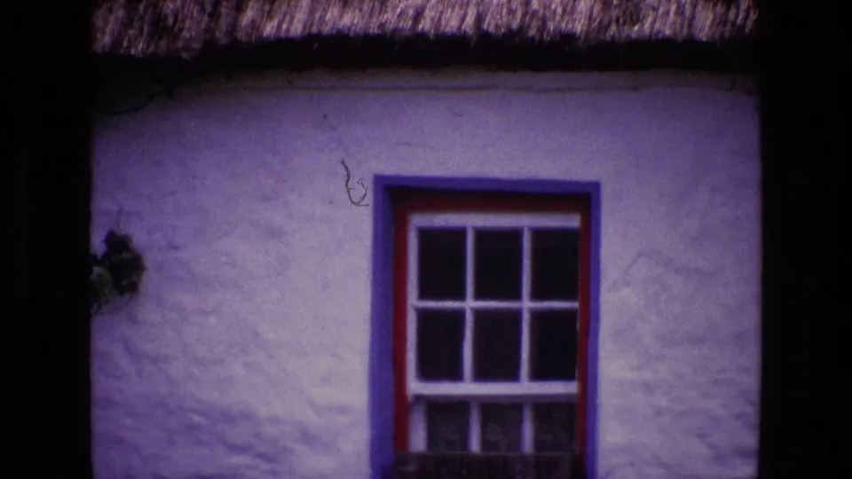 Soft 8mm frame of an Irish cottage window with red and blue paint, white stucco, and thatched roof detail.