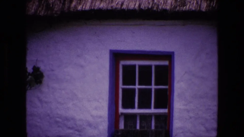 1969 Ireland 8mm frame showing a whitewashed thatched cottage wall with a red and blue framed window.