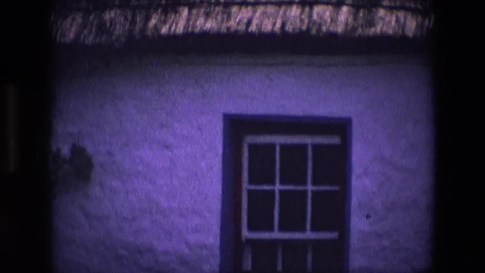 1969 Ireland home-movie frame of a whitewashed cottage window under thatch, with visible 8mm color shift.