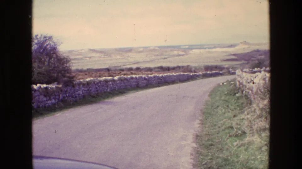 1969 Ireland 8mm view down a rural road between dry stone walls toward rolling open countryside.