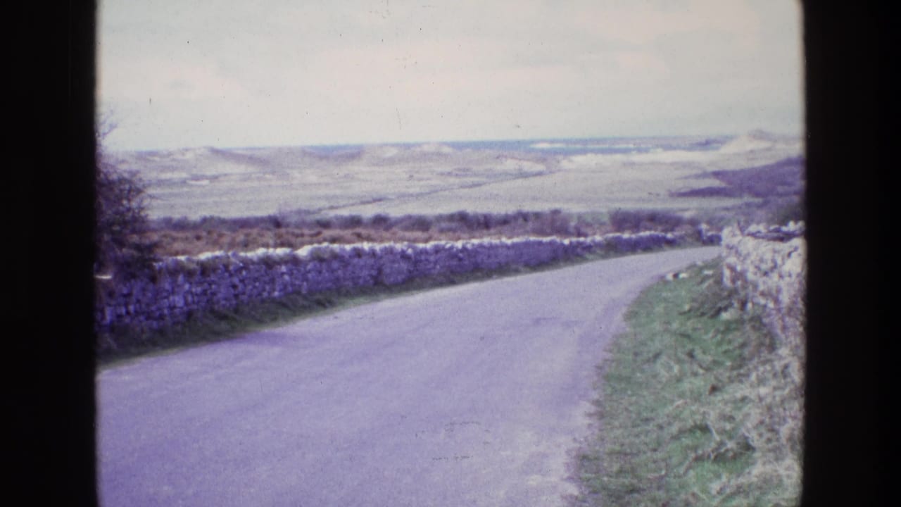 Rural road and stone walls leading toward distant hills with a purple film cast.