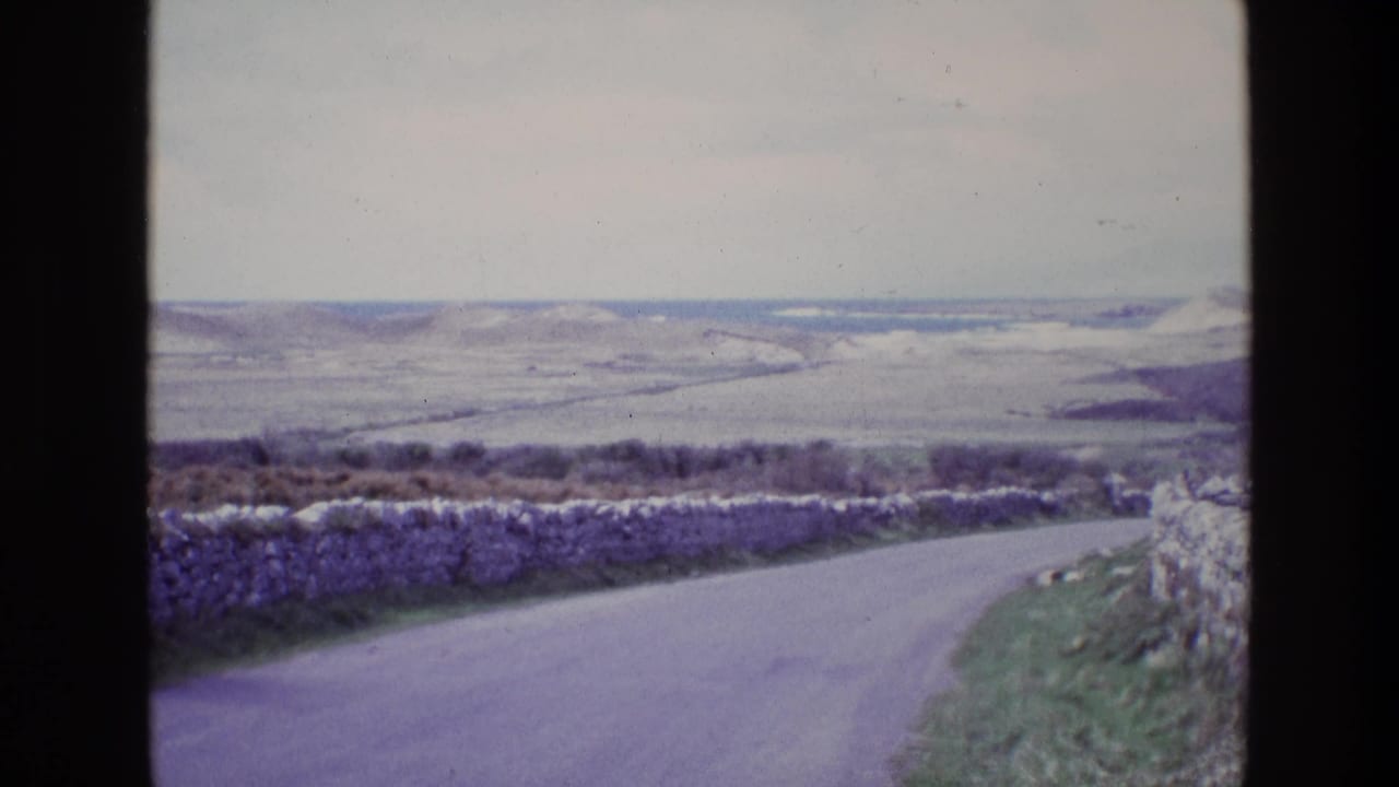 Curving road and stone wall leading toward distant open hills.