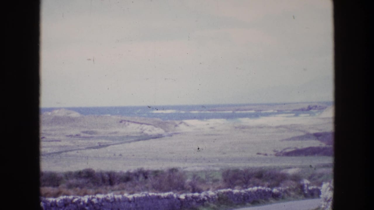 1969 Ireland home-movie frame showing rolling grasslands, distant surf, and a coastal horizon from a moving vehicle.