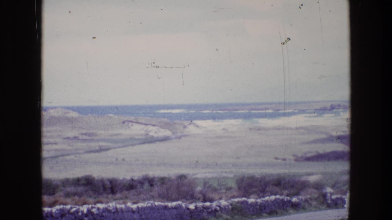 Wide coastal landscape with fields, shoreline, and dark window framing.