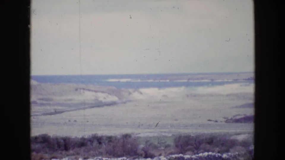 Muted 8mm frame from Ireland showing coastal grasslands, distant breaking waves, and heavy dark framing from a vehicle window.