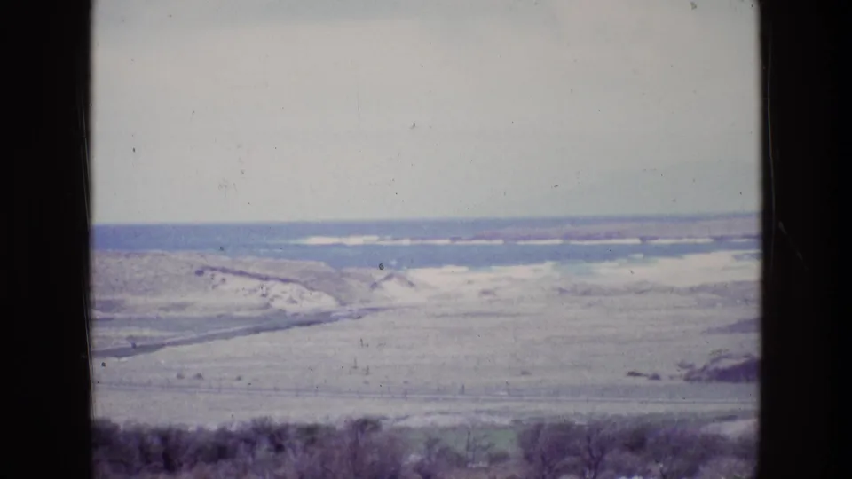 1969 8mm home-movie frame showing an Irish coastal landscape with dunes, grassland, breaking surf, and hazy sky.